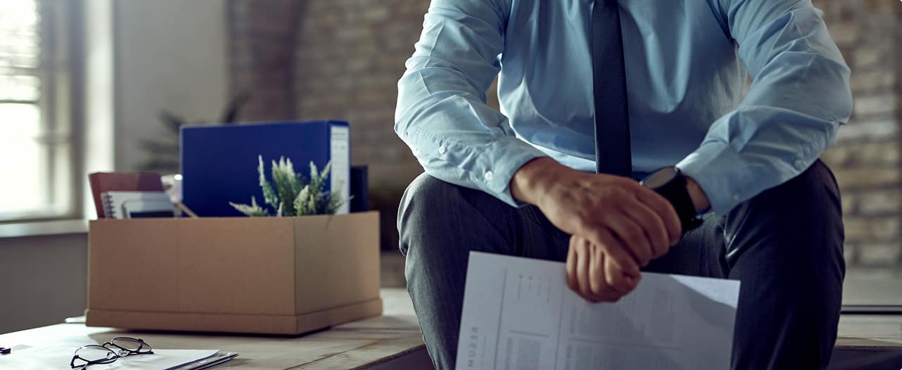 Trabalhador segurando caixa com pertences após demissão, analisando documento de rescisão